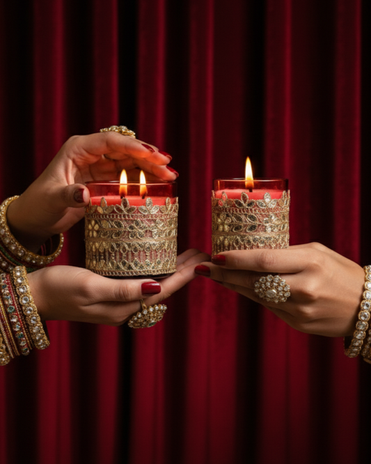 Two hands holding intricately designed candles against a red curtain background